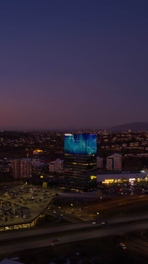 Turninn Smáratorgi rauð lýsing. Mynd af Turninum úr fjarska með blárri ljósasenu.